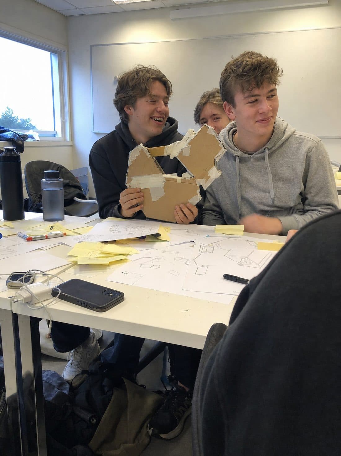 Elever ler sammen over skisser og en prototype i papp.